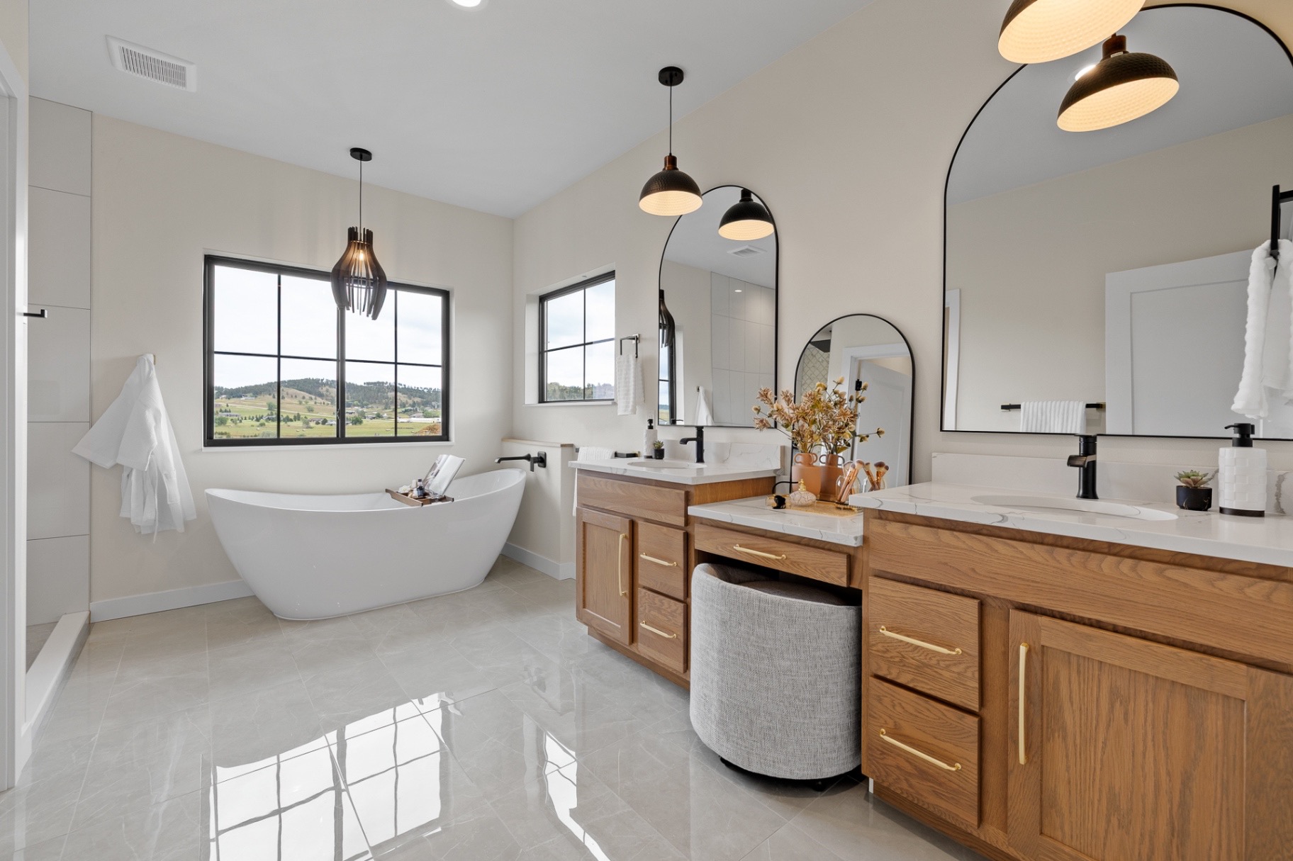 Primary bath with oak vanities, arched mirrors, freestanding tub and large format tile floors