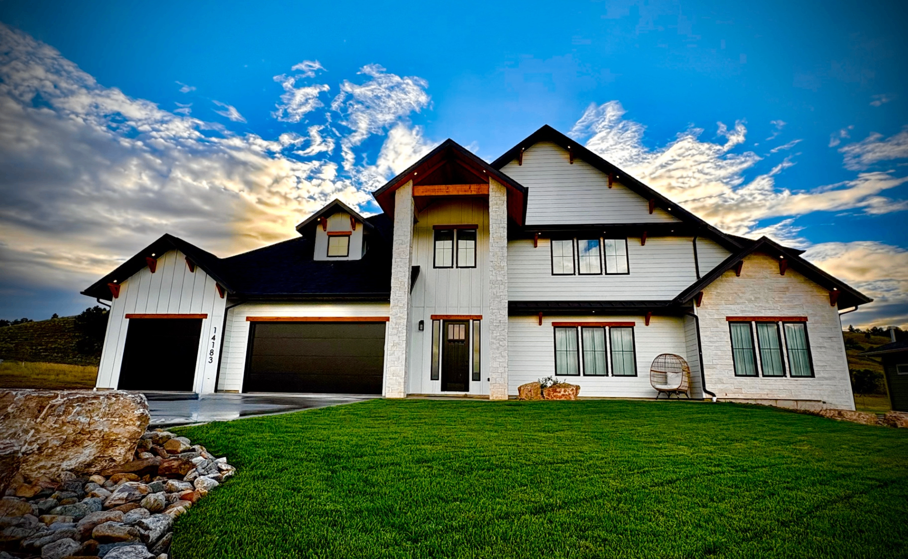 Front exterior of 14183 Saddle Hill Drive with white siding, stone gables, timber accents and black garage doors