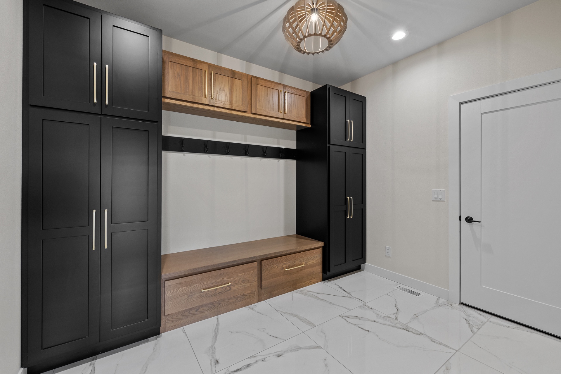 Mudroom with black painted lockers, white oak bench and upper cabinets on marble tile